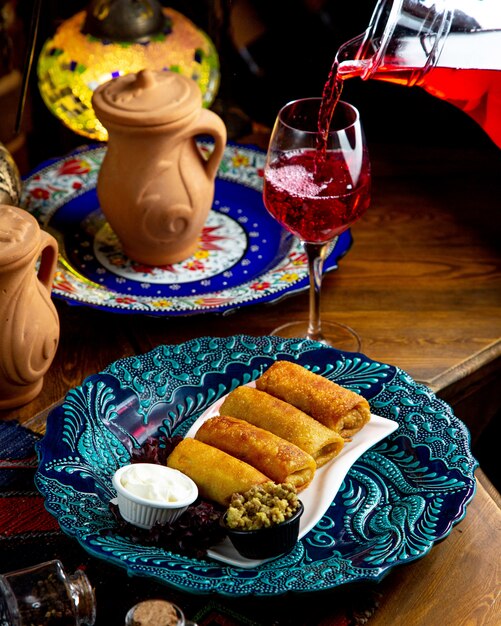 Side view of traditional russian pancake rolls with meat and sour cream and lemonade pouring in a glass on a wooden table