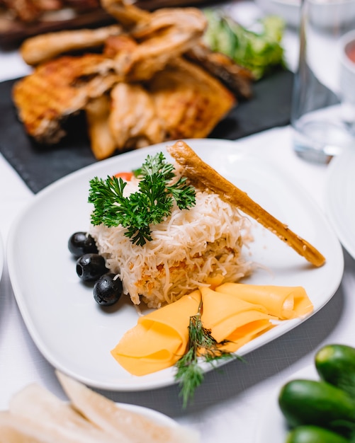 Side view of traditional russian salad mimosa with cannad fish potatoes cheese carrots and eggs decorated with black olives and fresh herbs on a white plate