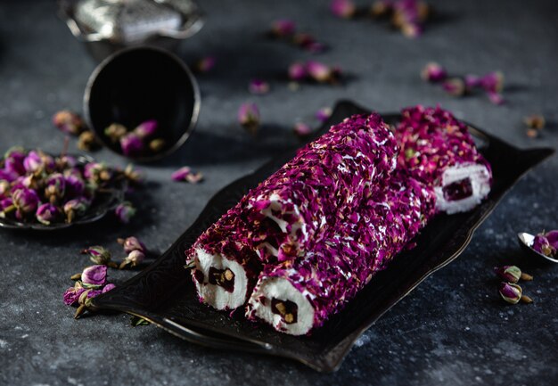 Side view of traditional turkish delight lokum with pistachios and rose flower on antique tray on black wall