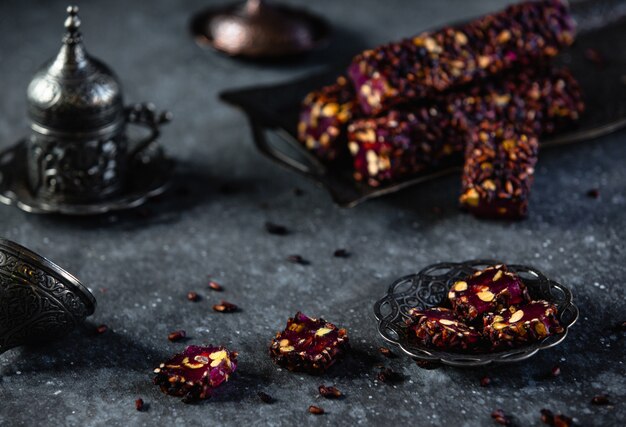 Side view of traditional turkish delight lokum with pistachios and rose flower on antique tray on black wall