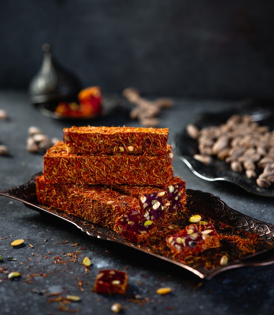 Side view of traditional turkish delight lukum with saffronpomegranate and pistachio on an antique tray on black wall