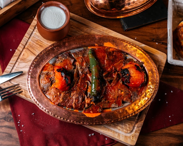 Side view of traditional turkish iskender doner with yogurt in a clay pot on a wooden board