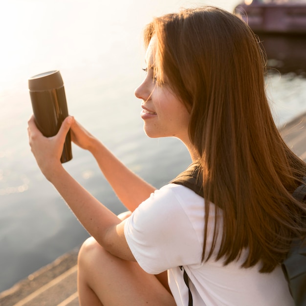 Side view of traveling woman by the river holding thermos