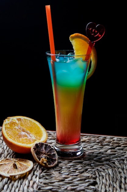 Side view tropical cocktail with tubules for beverages and dried orange in serving napkins on wooden table