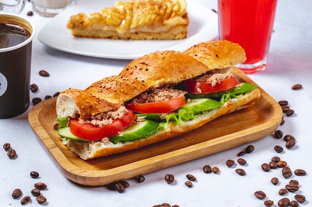 Боковой вид сэндвича с тунцом и белого хлеба с томатным салатом из огурцов и тунца и кофейных зерен на столе