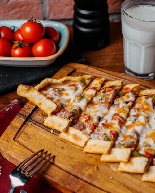 Side view of turkish pide with vegetables meat and cheese arranged on a wooden cutting board