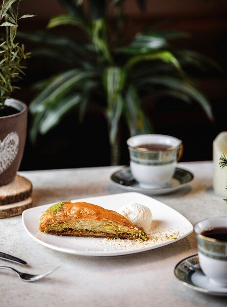 Side view of turkish sweets triangular shaped baklava with pistachio served with ice cream ball on plate