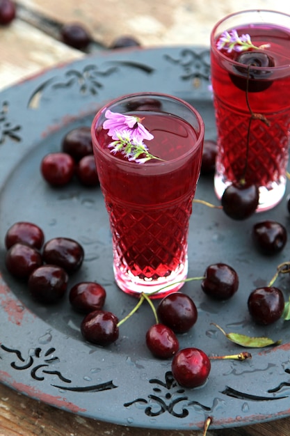 Free photo side view two cherry glasses of juice with cherries on tray