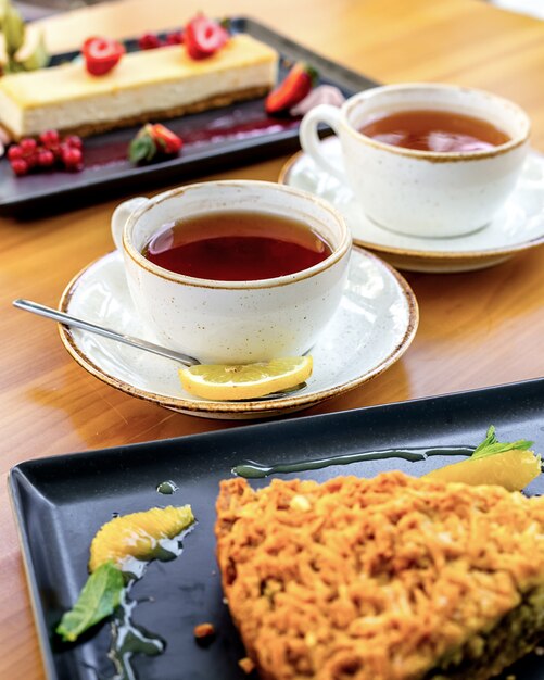 テーブルの上のレモンとデザートのスライスとお茶の2つのカップの側面図
