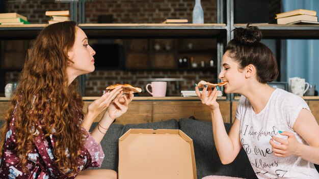 Side view of two female friends eating pizza