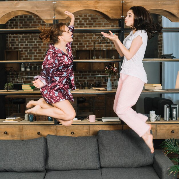 Side view of two female friends jumping on sofa