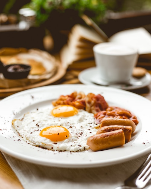 Side view two fried eggs with sausages beans and bacon on a plate