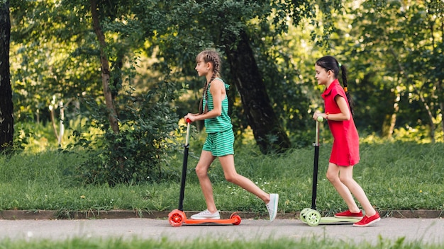 Side view of two girls riding push scooter in the park