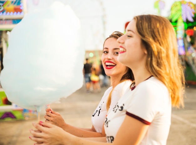 Free photo side view of two happy female friends holding blue candy floss