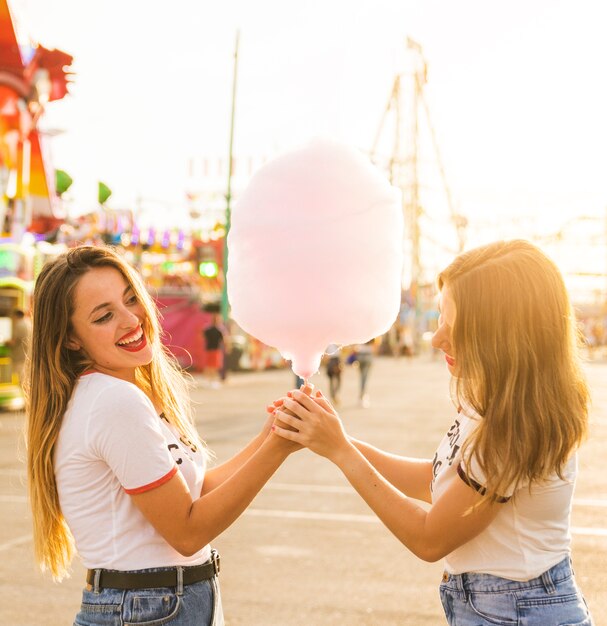 Una vista laterale di due amici femminili felici con zucchero filato rosa al parco di divertimenti