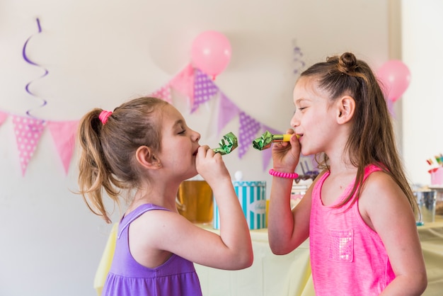 Side view of two little female friends blowing party horn