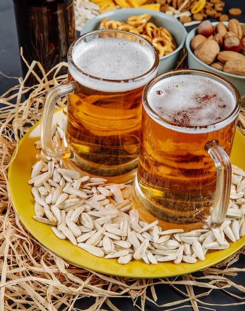Side view of two mugs of beer on a plate with sunflower seeds on straw