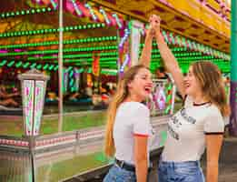 Free photo side view of two smiling female friends raising their arms