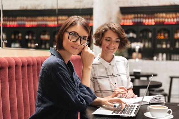 Вид сбоку двух улыбающихся женщин-менеджеров, сидящих за столом
