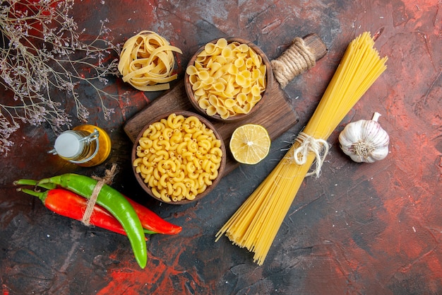 Side view of uncooked pastas on cutting board cayenne peppers tied in one another with rope oil bottle lemon or garlic on mixed color table footage