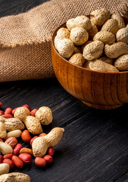 Side view unshelled peanuts in a bowl with peeled on a black wooden table