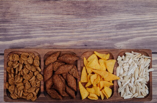 Side view of varied beer snacks bread crackers chips and sunflower seeds on a wood platter on rustic with copy space