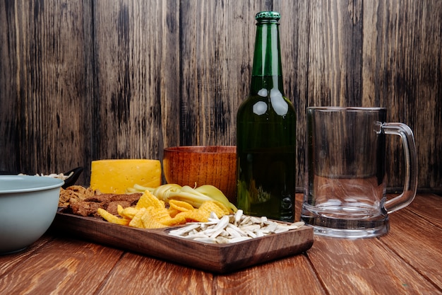 Side view of varied salty beer snacks on a wood platter with a bottle of beer on rustic wood