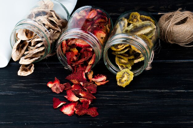 Side view of various dried fruit slices scattered from glass jars on black background