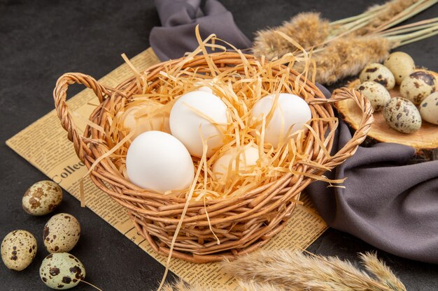 Side view of various organic eggs in a brown pot on a wooden board on an old newspaper spike black towel on dark surface