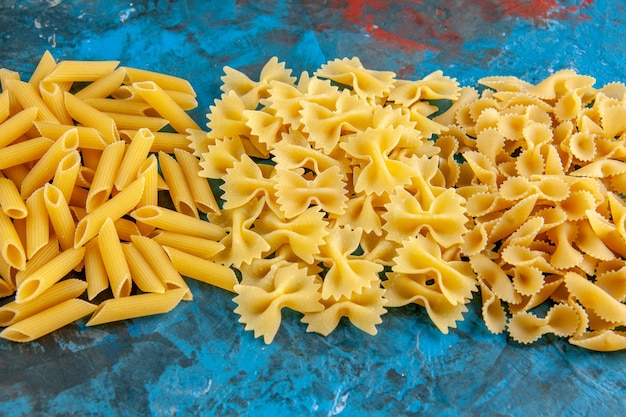 Side view of various raw Italian pastas arranged in a row on blue background