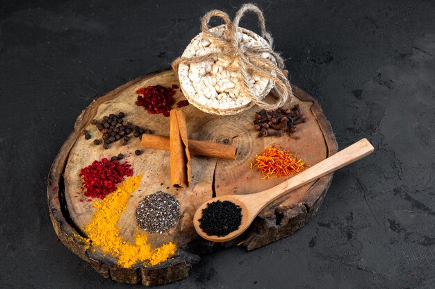 Side view of various spices a wooden spoon with black seeds and rice breads tied with a rope on wooden board on black