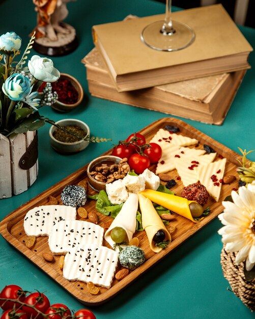 Side view of various types of cheese with nuts grapes and cherry tonatoes on wooden platter