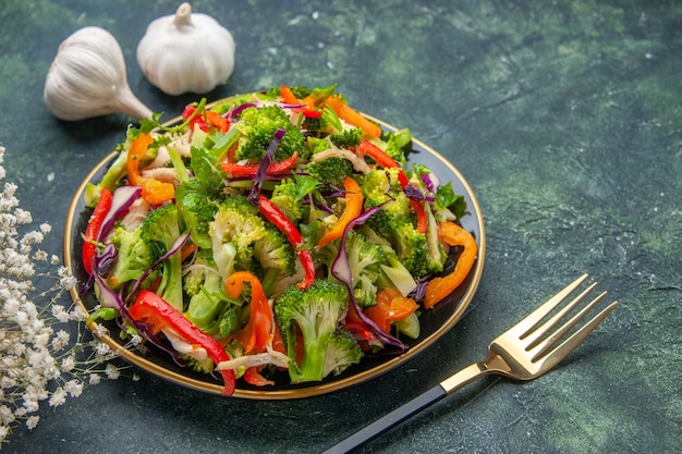 Vista laterale dell'insalata vegana in un piatto e forchetta all'aglio fiore bianco su sfondo scuro