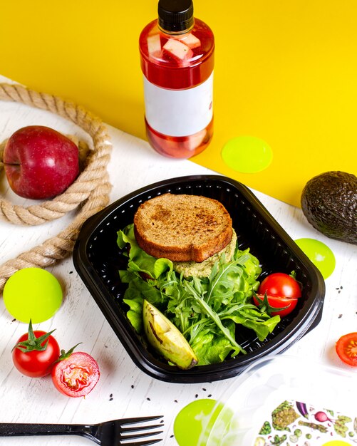 Side view of vegan sandwich with avocado and tomatoes in delivery box