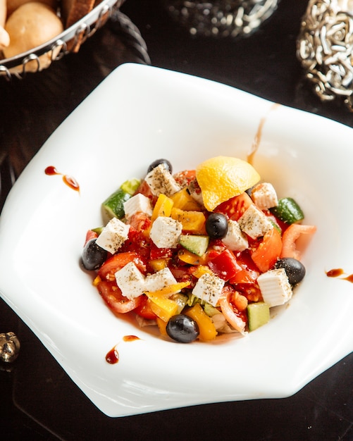 Side view of vegetable salad with feta cheese and olives in a white plate