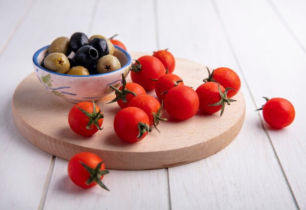 Side view of vegetables as bowl of olive and tomatoes on cutting board on wood
