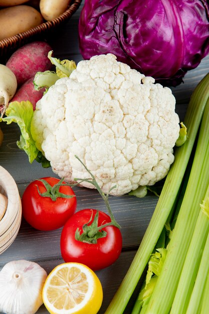 Side view of vegetables as cauliflower celery tomato cabbage garlic with cut lemon on wooden background