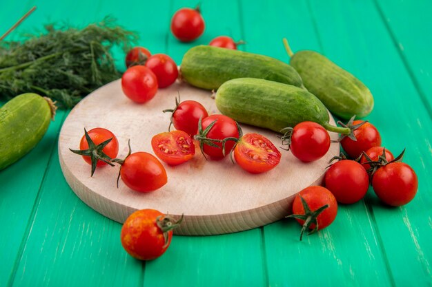 Side view of vegetables as cucumber and tomato on cutting board and bunch of dill on green