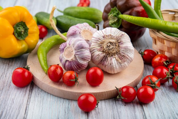 Side view of vegetables as garlic tomato on cutting board with cucumber pepper on wood