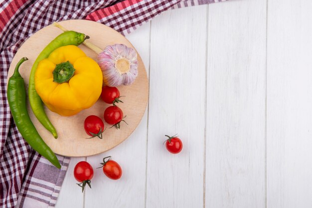 Side view of vegetables as garlic tomato pepper on cutting board on plaid cloth on wood with copy space