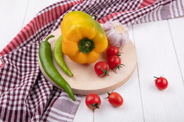 Side view of vegetables as garlic tomato pepper on cutting board on plaid cloth on wood