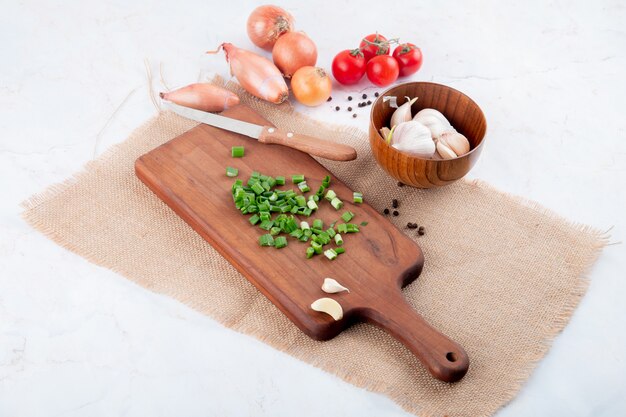 Side view of vegetables as green onion on cutting board garlic tomato with knife on white background with copy space