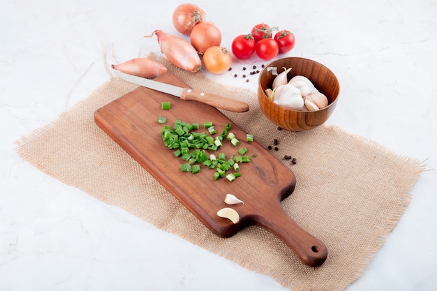 Side view of vegetables as green onion on cutting board garlic tomato with knife on white background with copy space