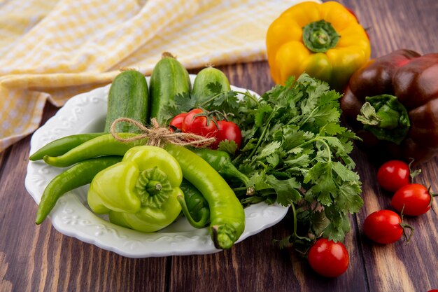 Side view of vegetables as pepper coriander cucumber in plate and plaid cloth with tomatoes on wood