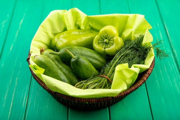 Side view of vegetables as pepper cucumber dill in basket on green