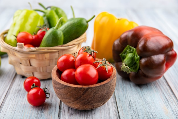 Side view of vegetables as pepper cucumber tomato in basket bowl and on wood