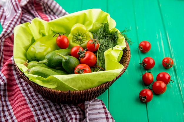 Side view of vegetables as pepper tomato cucumber dill in basket on plaid cloth and green