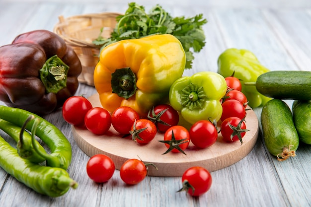 Side view of vegetables as pepper and tomato on cutting board with cucumber and dill on wood