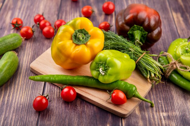 Side view of vegetables as peppers and dill on cutting board with cucumbers tomatoes and knife on wood