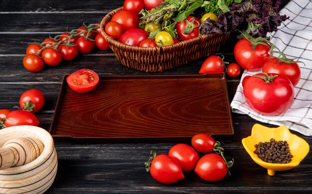 Вид сбоку овощей, как томатный зеленый мяты листья базилика в корзине и нарезанный помидор в лотке черный перец чеснок дробилка на деревянный стол